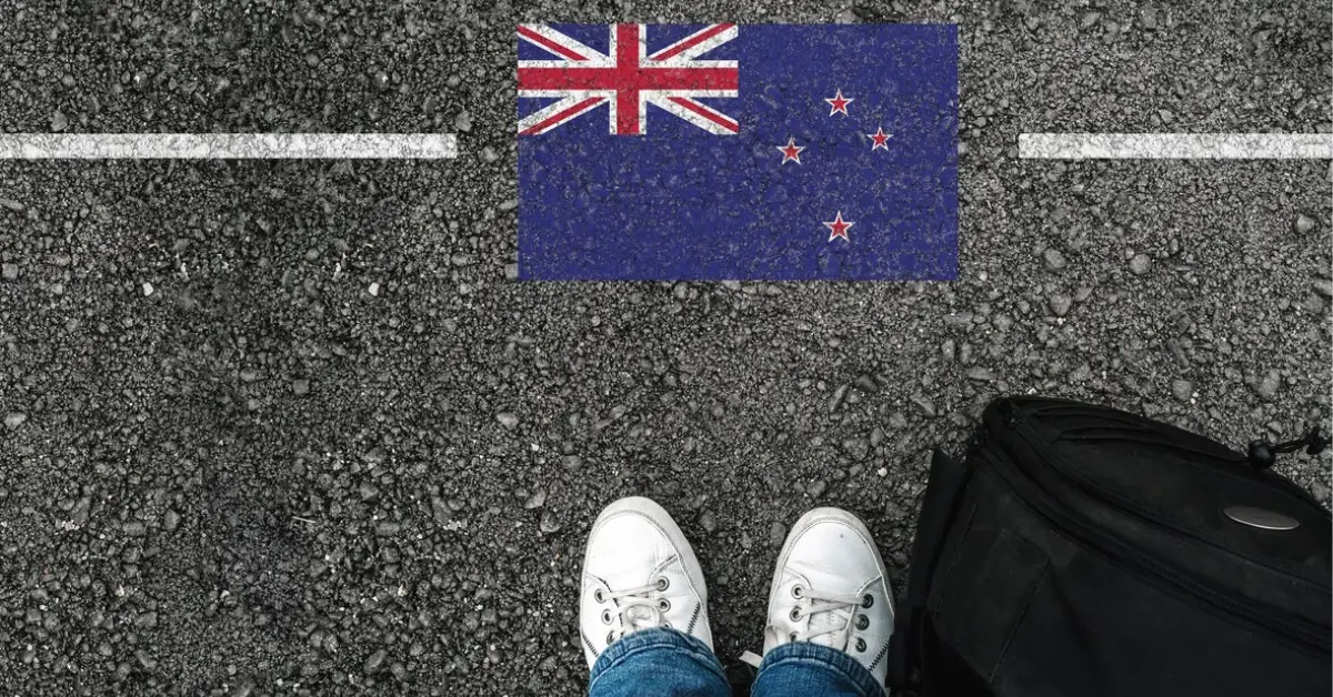 A man with a travel bag near new zealand flag